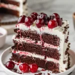 Slice of moist Black Forest Cake topped with cherries and whipped cream.
