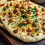 Crispy chickpea flatbread served on a wooden platter with fresh herbs.