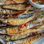 A plate of crispy fried dried fish served with dipping sauce.