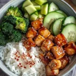Glazed chicken rice bowl with broccoli and cucumber on a white plate