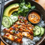 Spicy honey-ginger chicken bowl garnished with yum yum sauce and fresh vegetables
